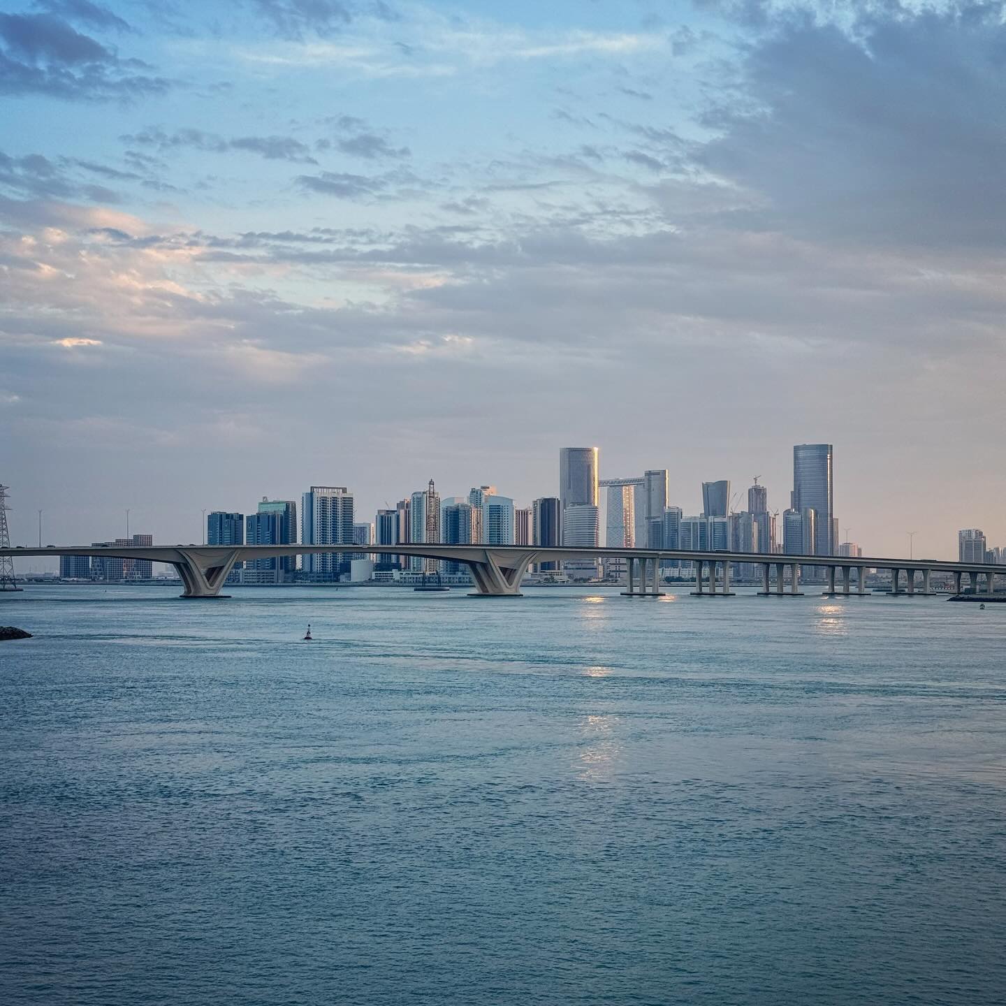 A distant skyline of towers beyond calm blue water.