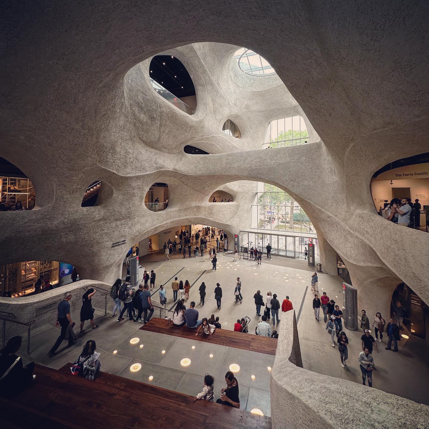 Curving pale walls and irregular openings frame the museum’s busy central space.