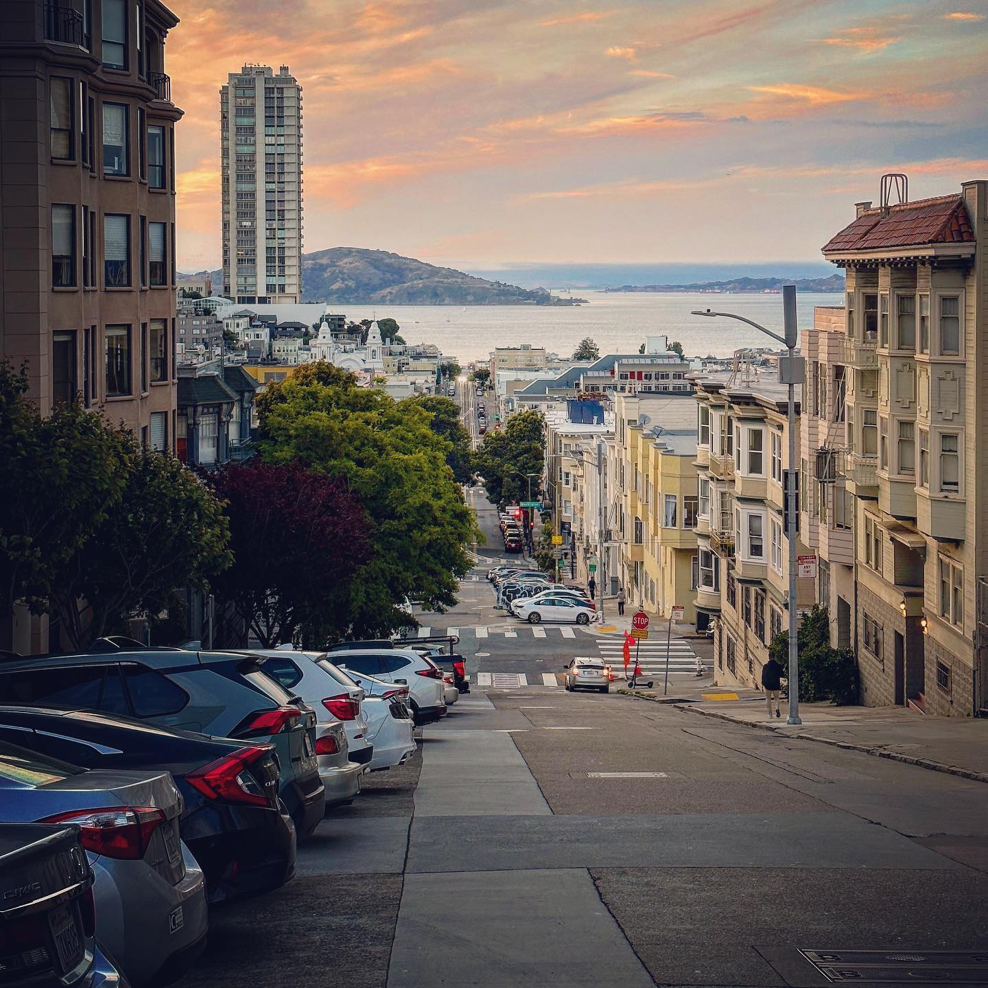 A steep residential street descends towards the water in evening light.