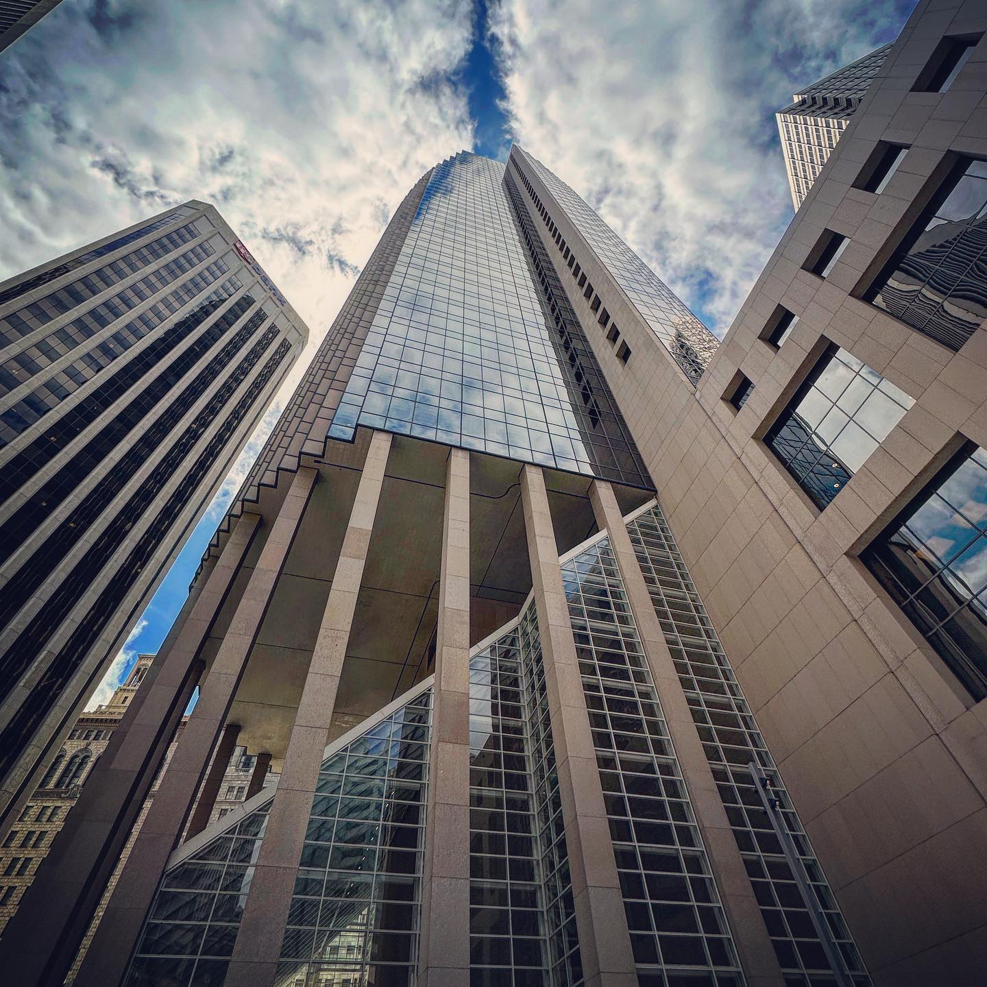A tall glazed tower framed by neighbouring façades and clouds.