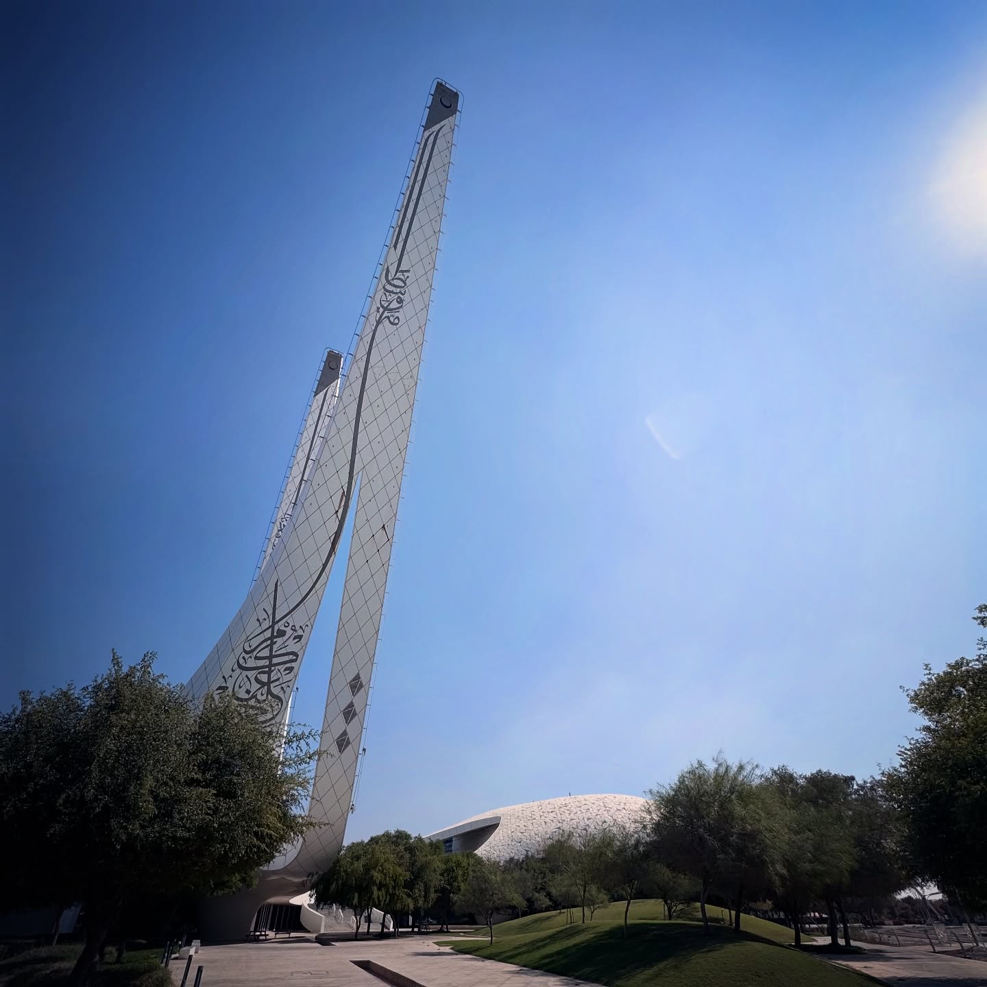 Two slender minarets rise at an angle into a clear blue sky.