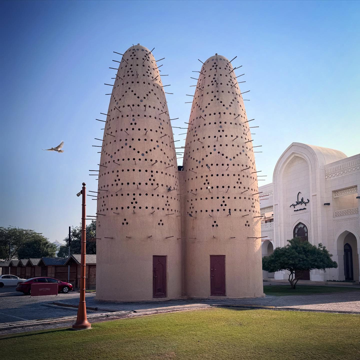 Two textured pigeon towers beside a white building and lawn at Katara Cultural Village.