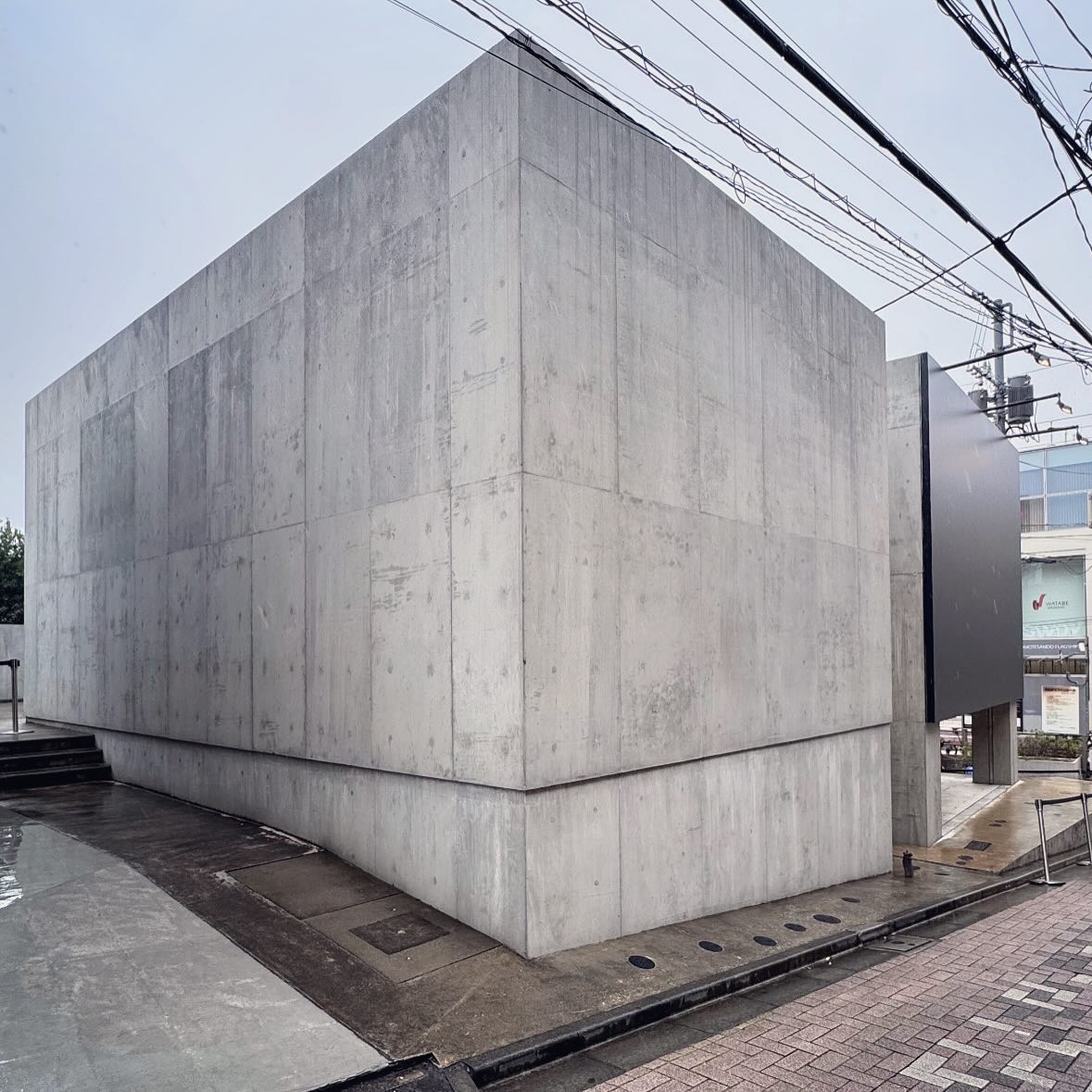 A quiet concrete gallery façade beside a narrow street and overhead wires.