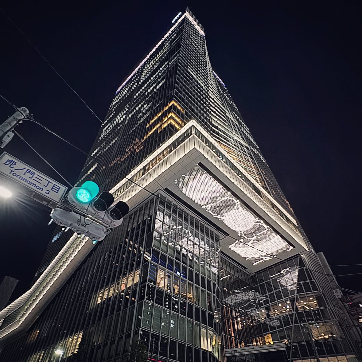 A layered tower and illuminated projecting floors seen from a Tokyo intersection.