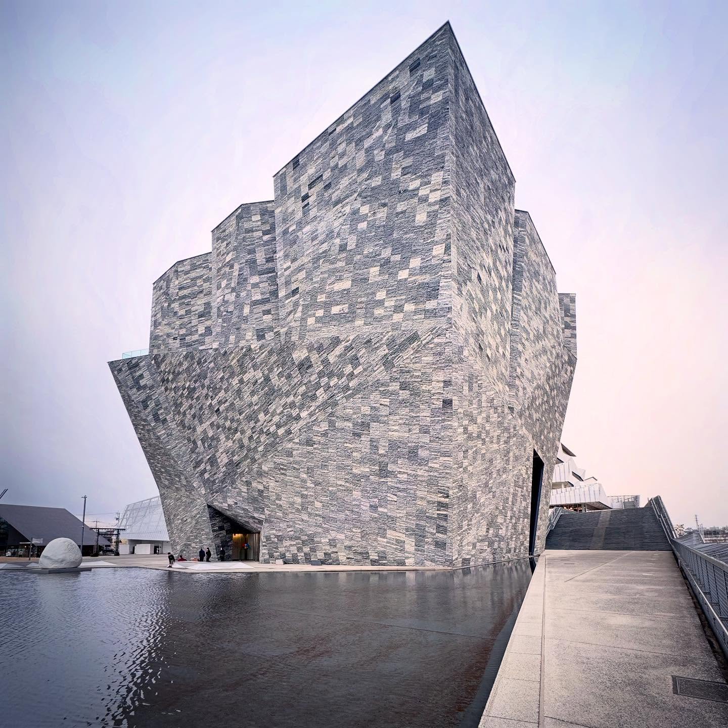A monumental, angular stone-clad museum rising from a paved forecourt.