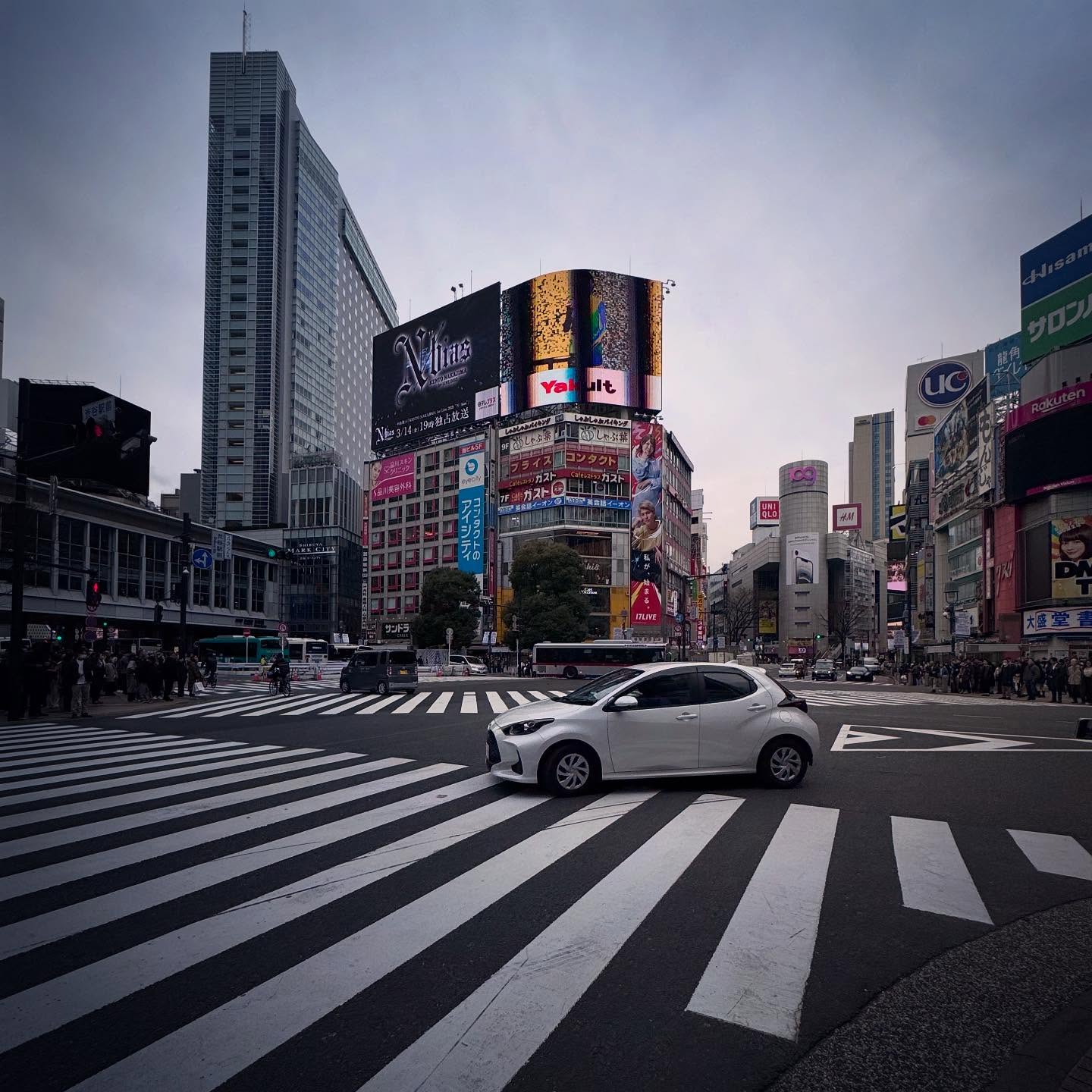 The diagonal geometry of Shibuya Crossing beneath large urban signs.