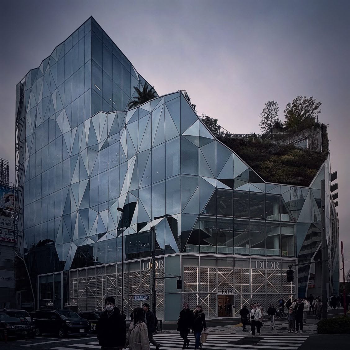 A faceted glass façade with triangular surfaces on a Japanese shopping street.