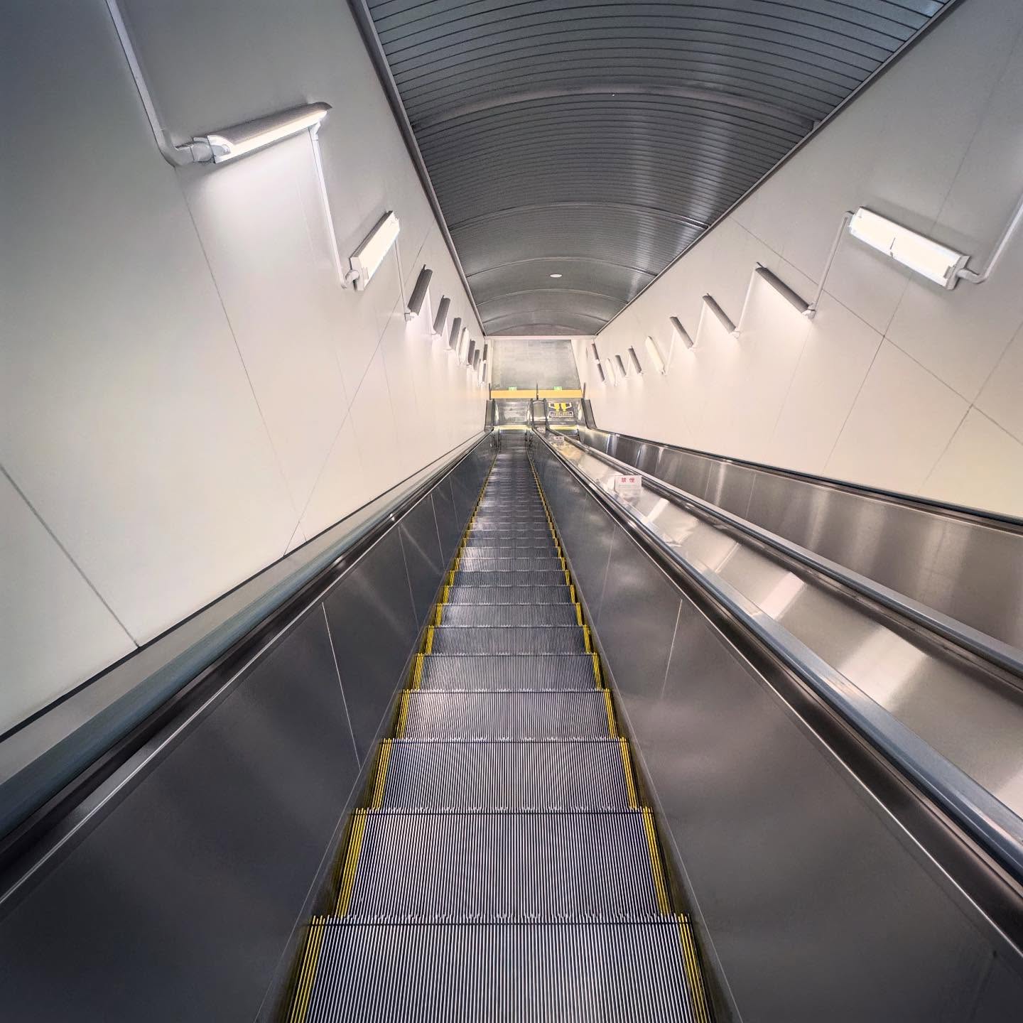 An escalator descending through a long, brightly lit passage.