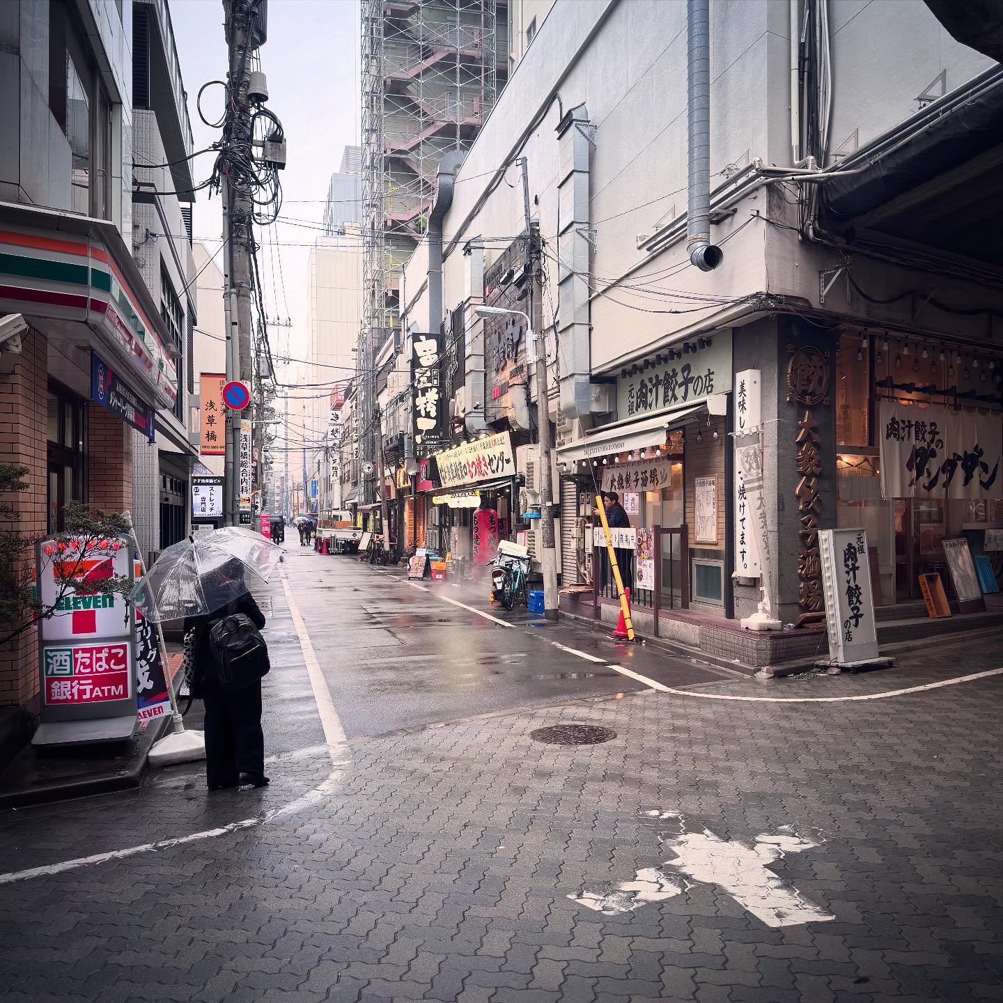 A gently curving street with closely spaced shops, signs and overhead cables.