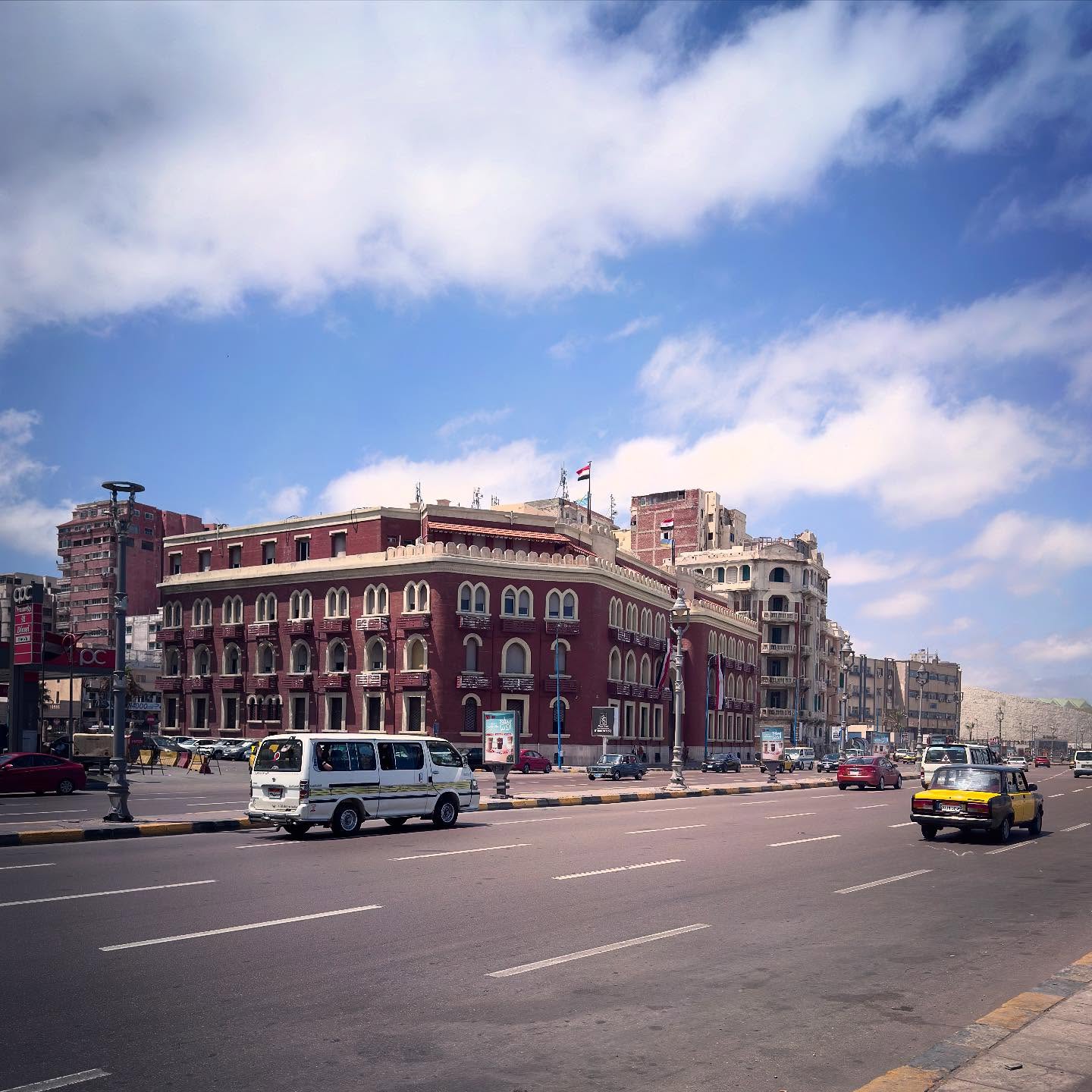 A red historic corner building and neighbouring façades beside a broad city street.