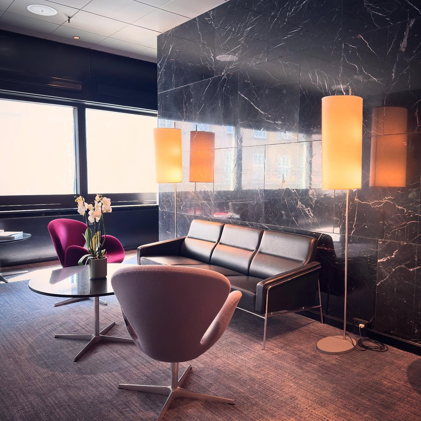 Lounge chairs, a dark sofa and warm pendant lights against veined stone.