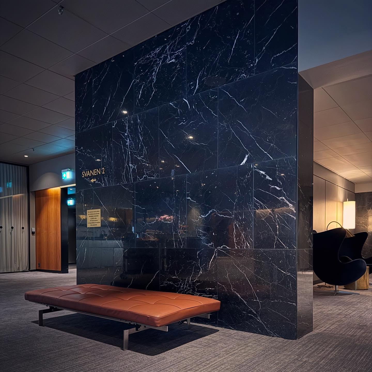 A slim bench against a tall dark marble wall.