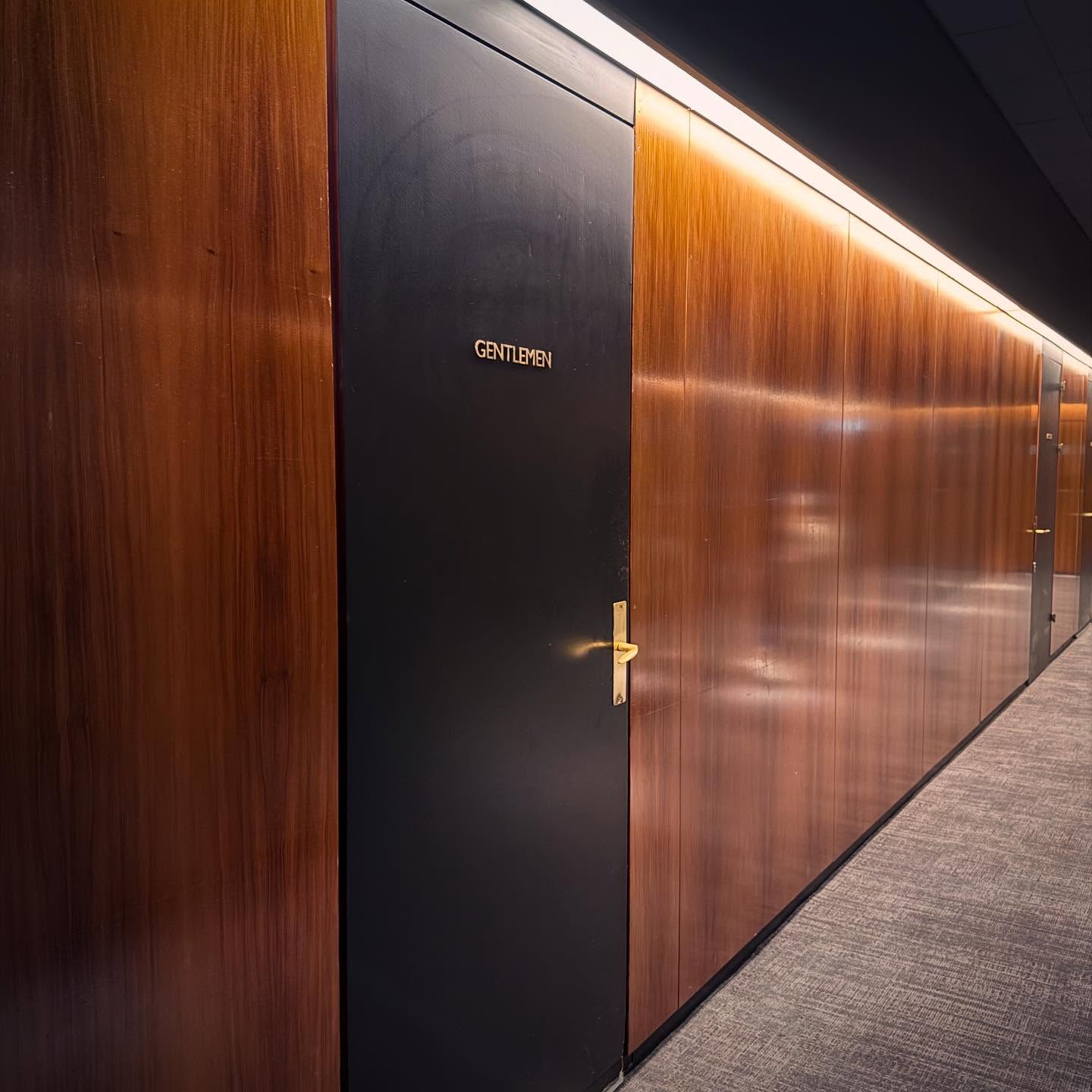 A softly illuminated timber corridor wall leading towards a dark doorway.