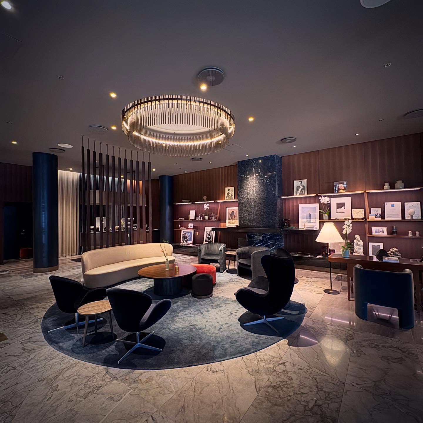 A lounge with curved seating, a circular rug and a suspended light at the Radisson Collection Royal Hotel.