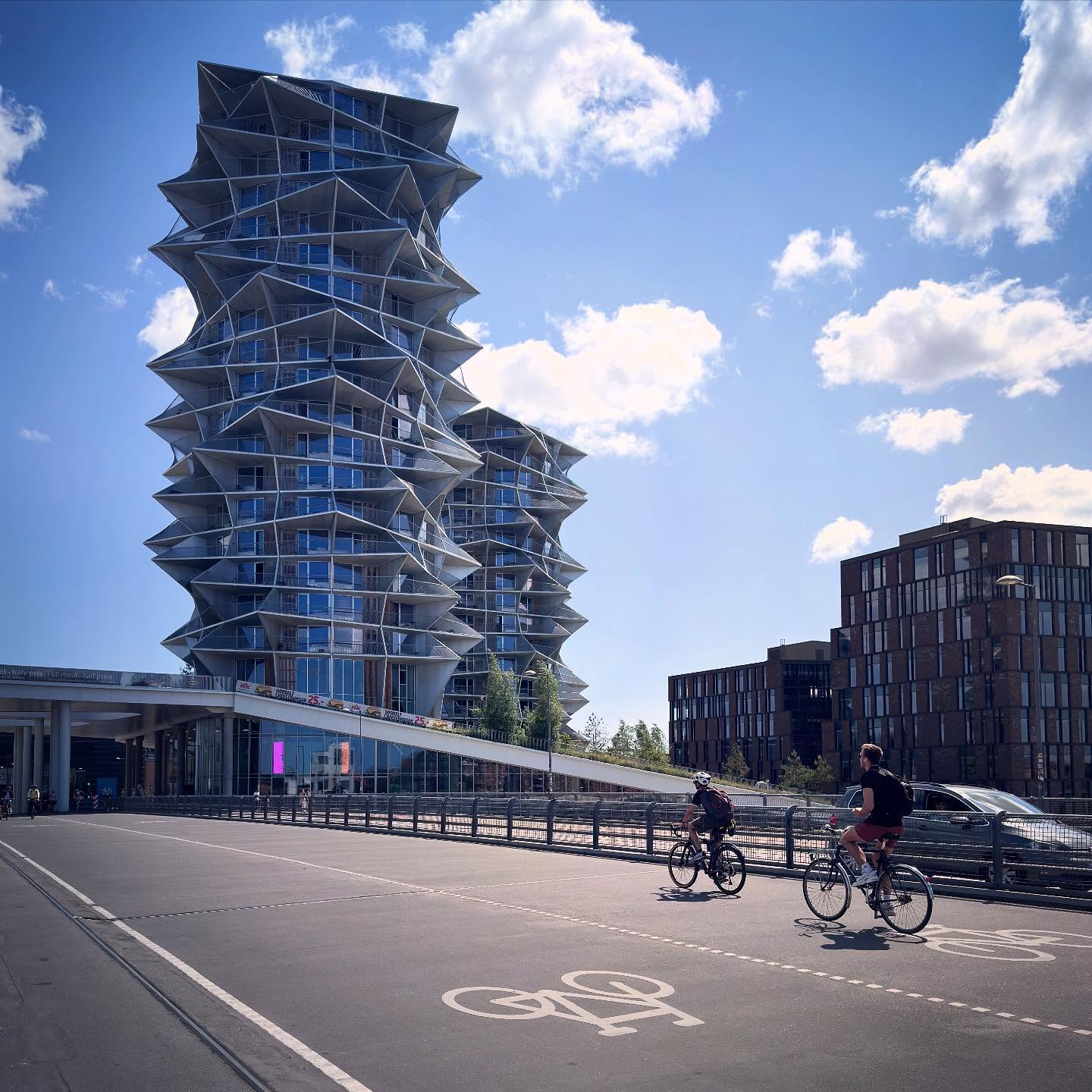 Angular residential towers above a broad cycle route and passing cyclists.