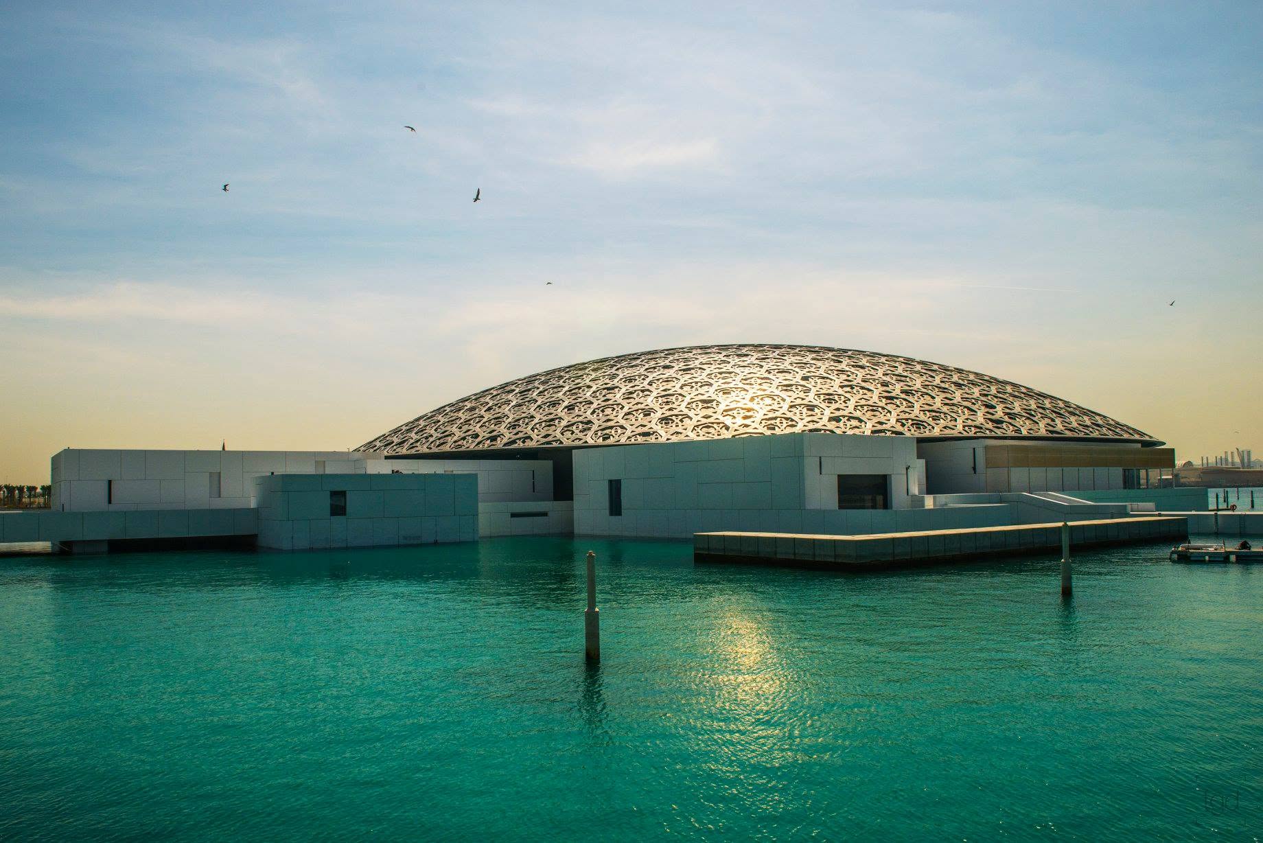 Louvre Abu Dhabi’s patterned dome above low white volumes and turquoise water.